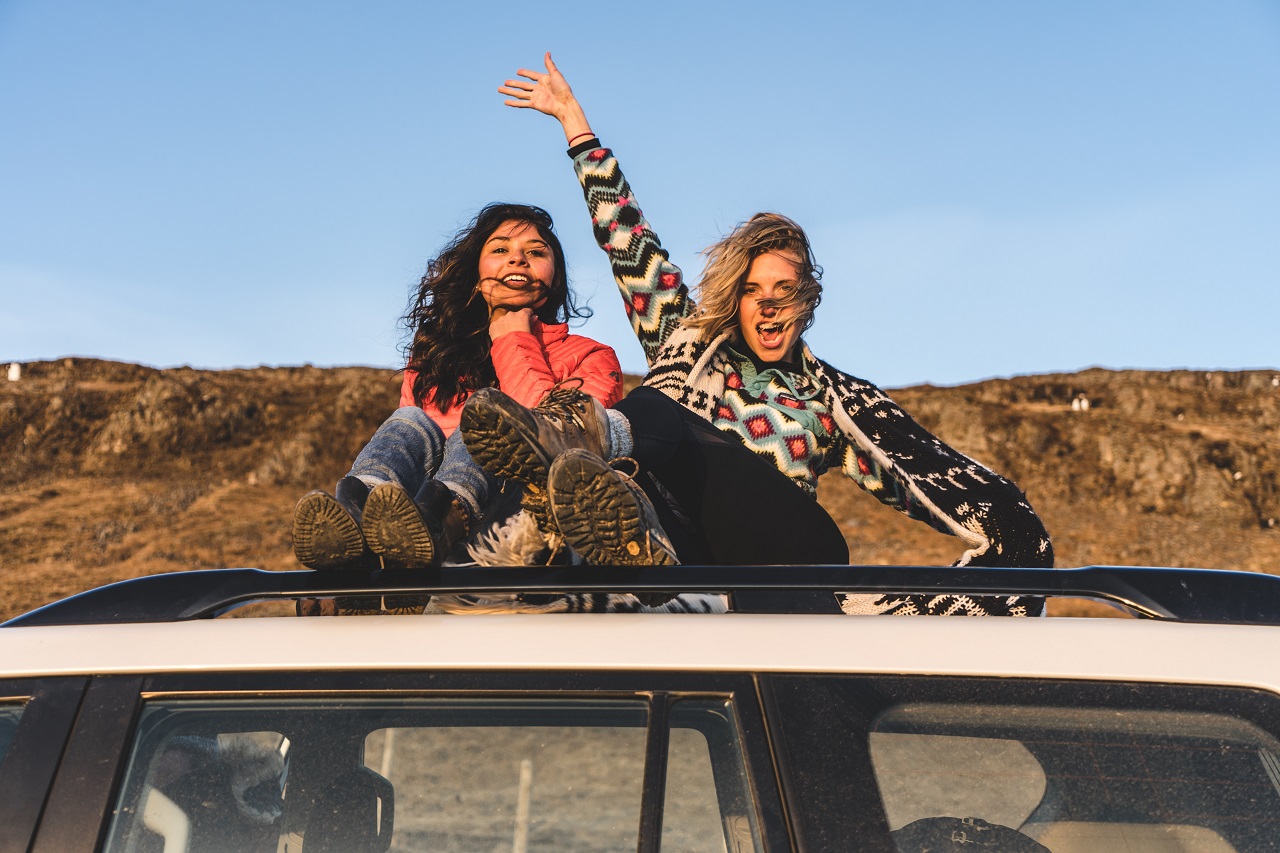 Zwei Frauen sitzen auf einem Autodach in den Bergen und Winken